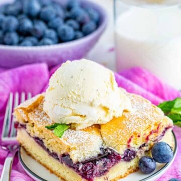 A blueberry bar topped with a scoop of vanilla ice cream on a plate with fresh blueberries.