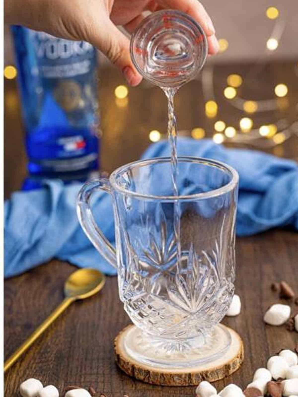 Shot of vodka being poured into the bottom of a glass mug.