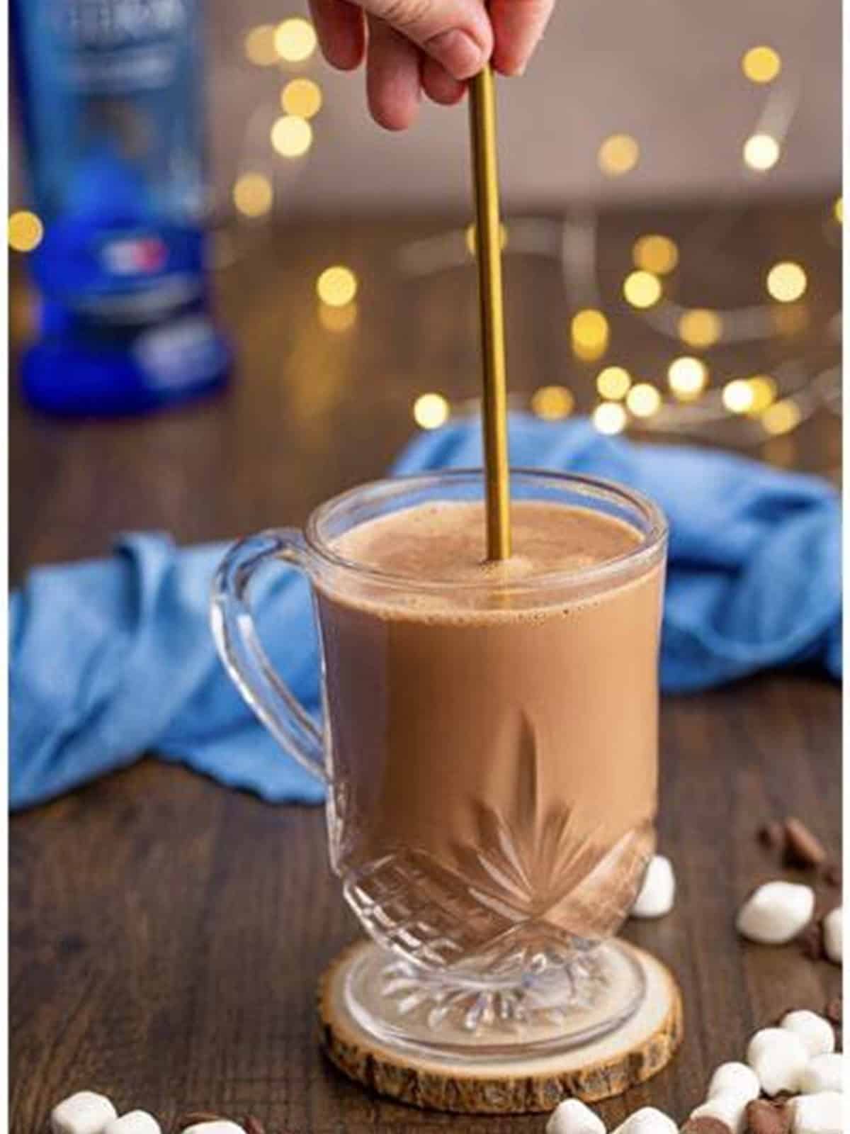 Boozy hot chocolate being stirred together in a glass mug with a gold spoon.