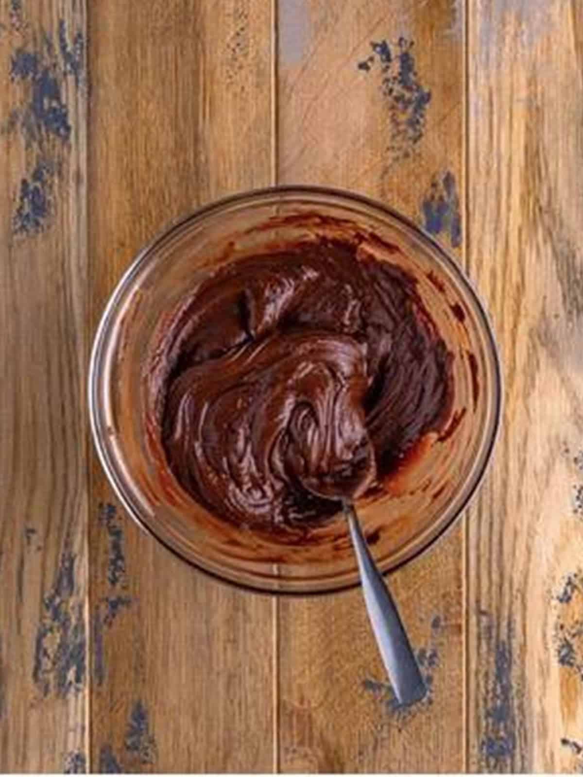 Melted chocolate chips and butter stirred smooth in a glass bowl for Brownie Cookies.