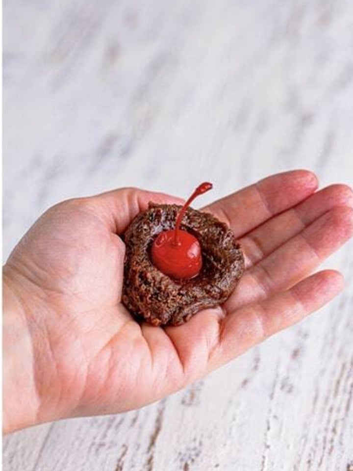 A maraschino cherry pressed into an indentation in the brownie mixture in a palm.