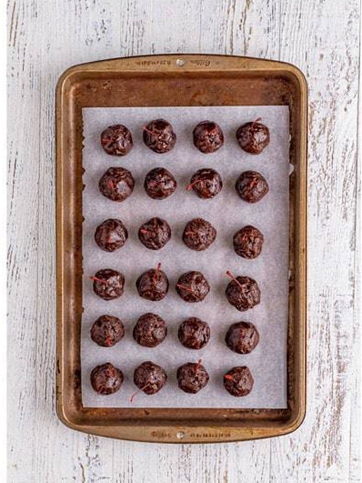 Brownie truffle balls lined up on a parchment lined tray headed to the freezer.