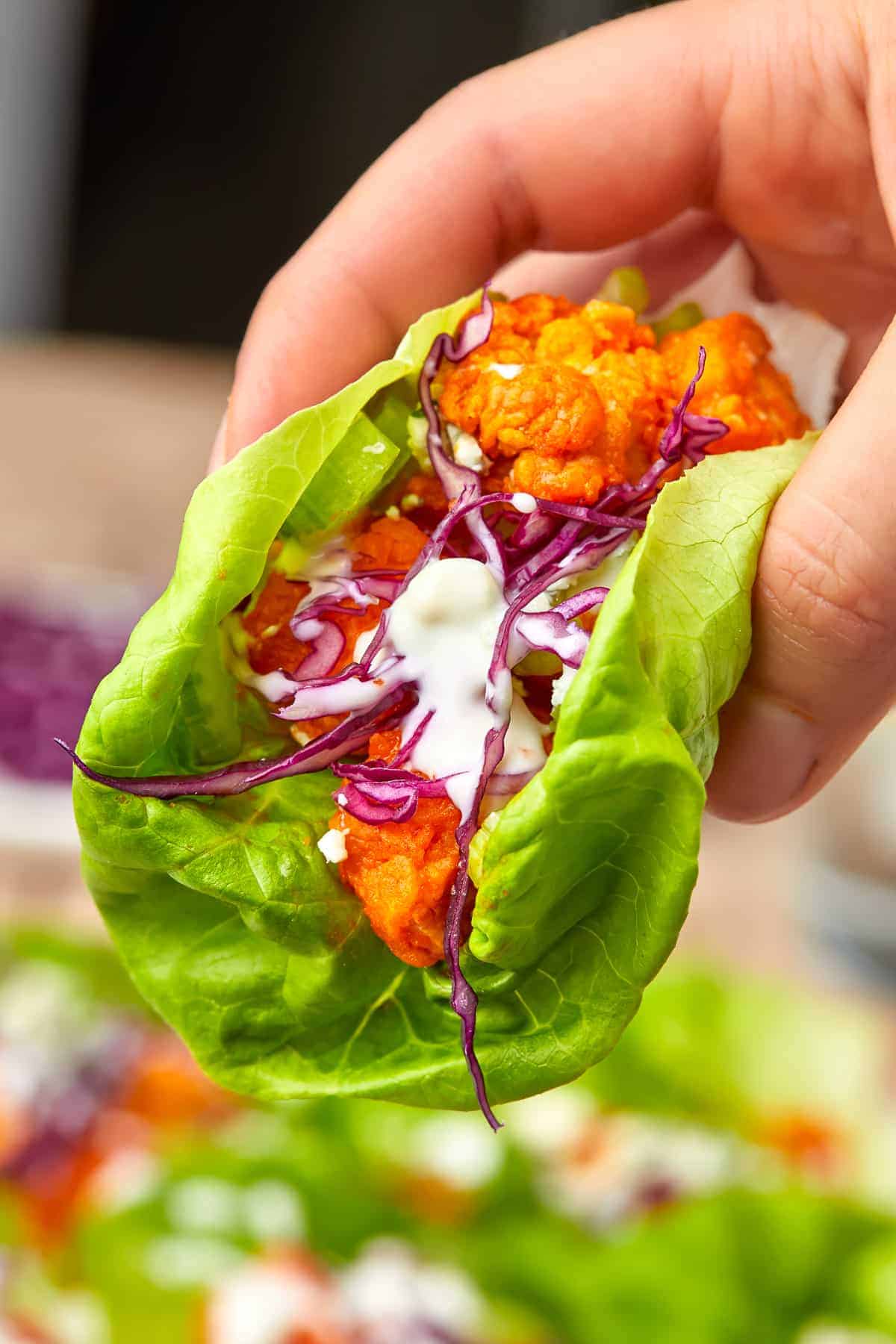 A hand holding a buffalo chicken lettuce wrap loaded with saucy chicken, cabbage, and blue cheese dressing.