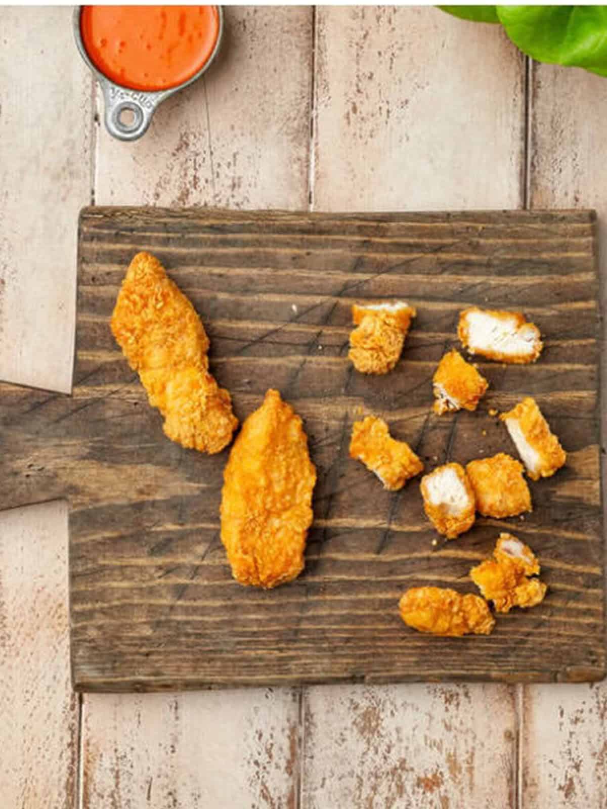 Crispy chicken tenders cut into bite-sized pieces on a cutting board for buffalo chicken lettuce wraps.