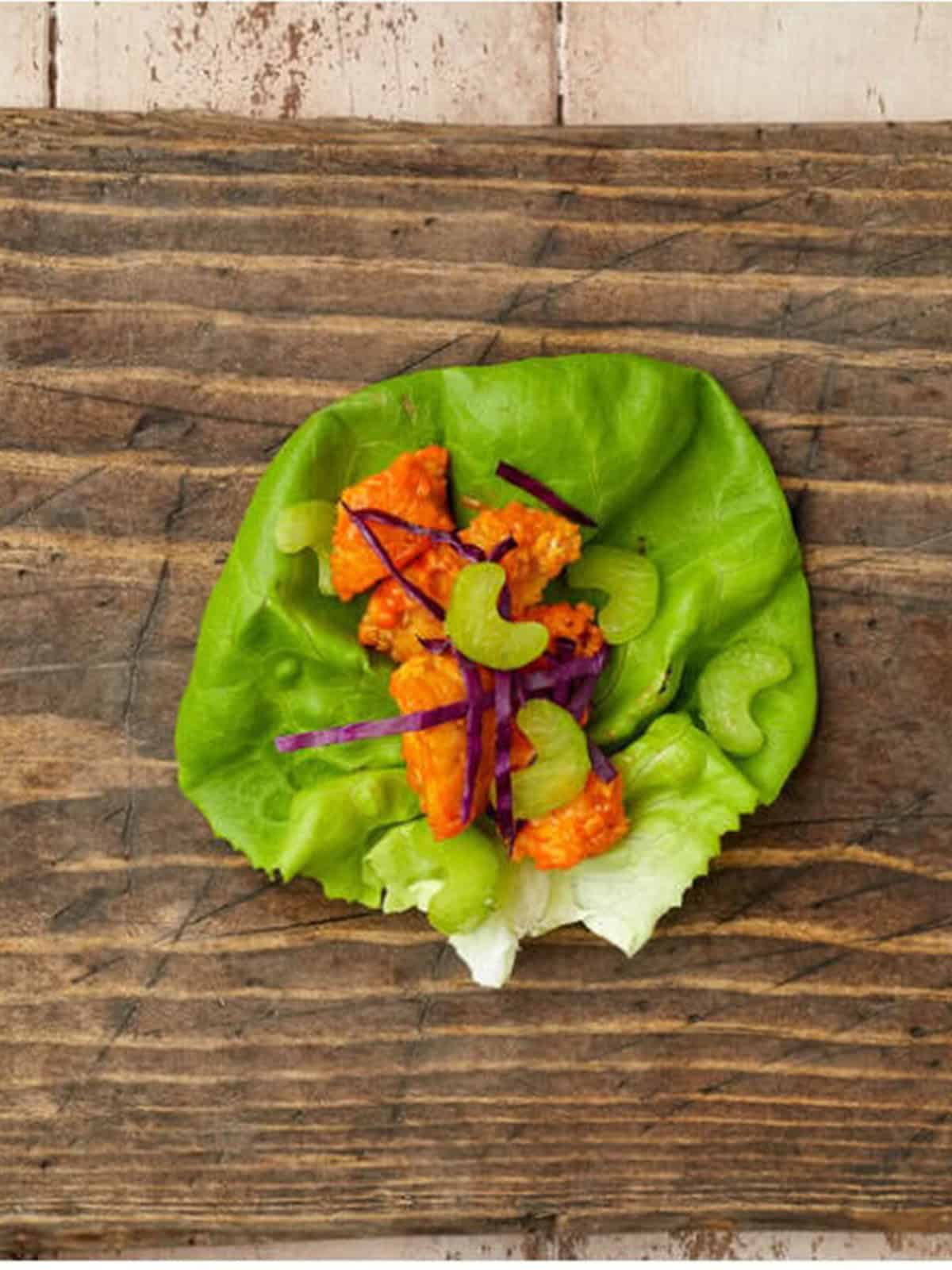 A butter lettuce leaf filled with buffalo chicken, red cabbage, and celery.
