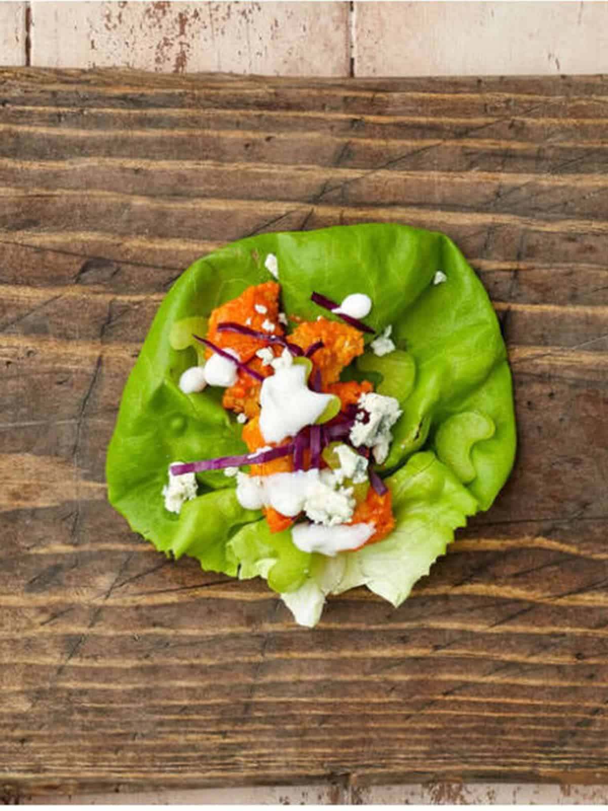 A finished buffalo chicken lettuce wrap topped with blue cheese dressing and blue cheese crumbles.