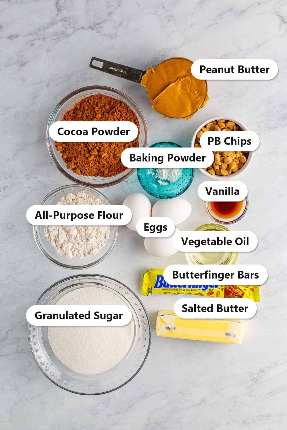 Labeled ingredients for Butterfinger brownies including cocoa powder, flour, sugar, eggs, peanut butter, peanut butter chips, and Butterfinger candy bars.