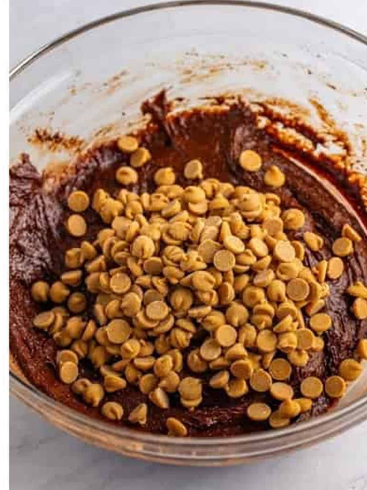 Peanut butter chips added on top of chocolate brownie batter in a glass bowl.