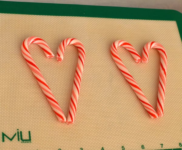 Candy canes arranged into heart shapes on a silicone baking mat before going into the oven.