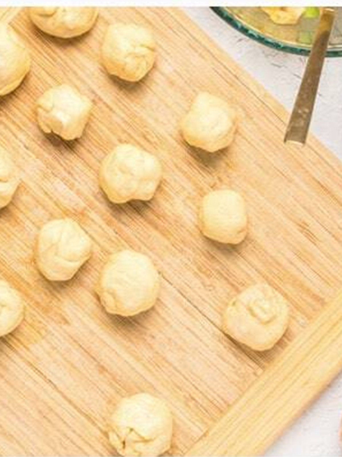 Sealed dough balls filled with caramel apple lined up on a board before frying.