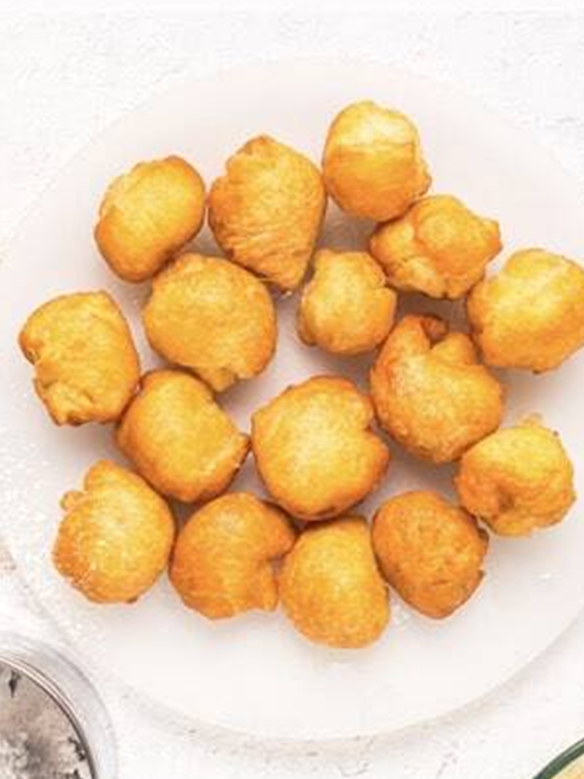 Golden brown caramel apple donut holes fried and draining on a plate.