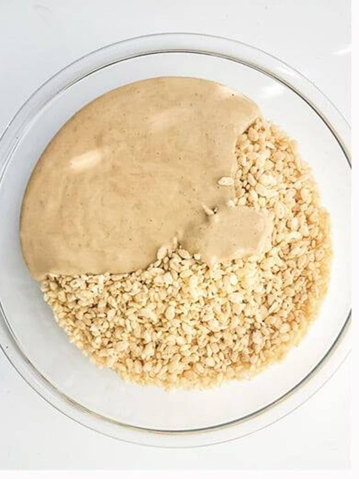 Melted marshmallow mixture poured over rice krispie cereal in a glass bowl.