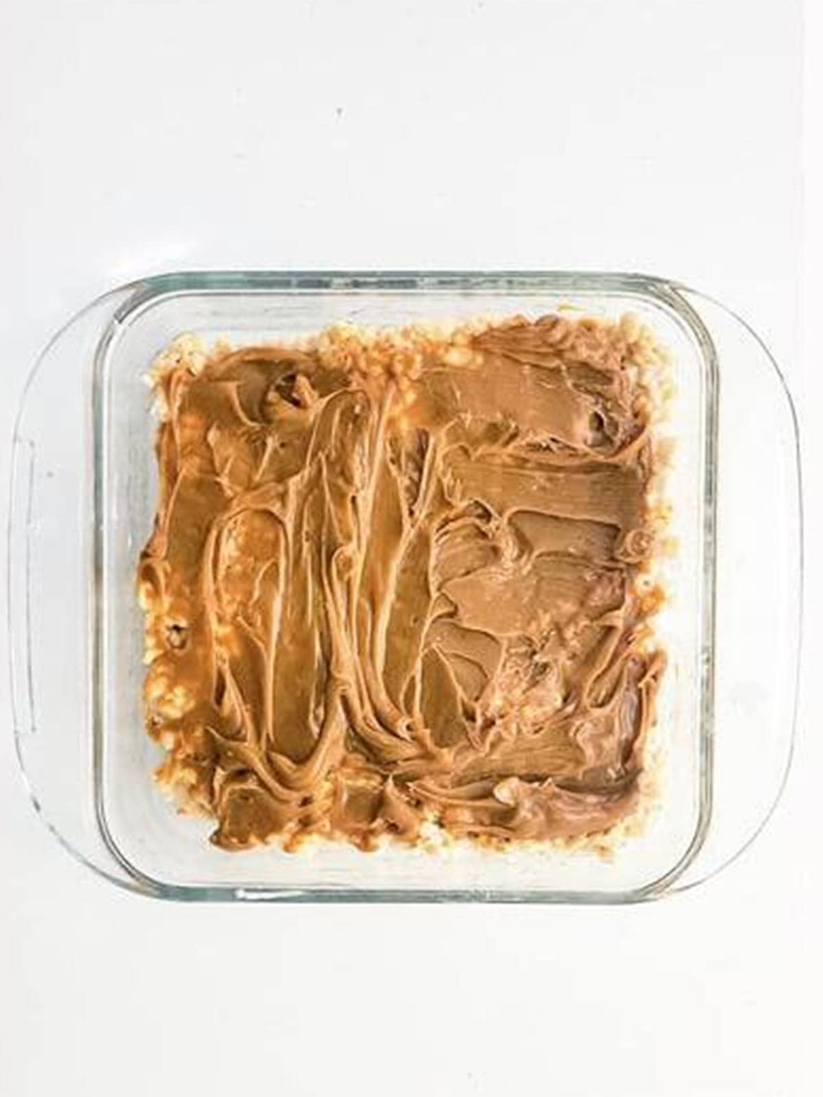 Dulce de leche spread in an even layer over the pressed rice krispie base.
