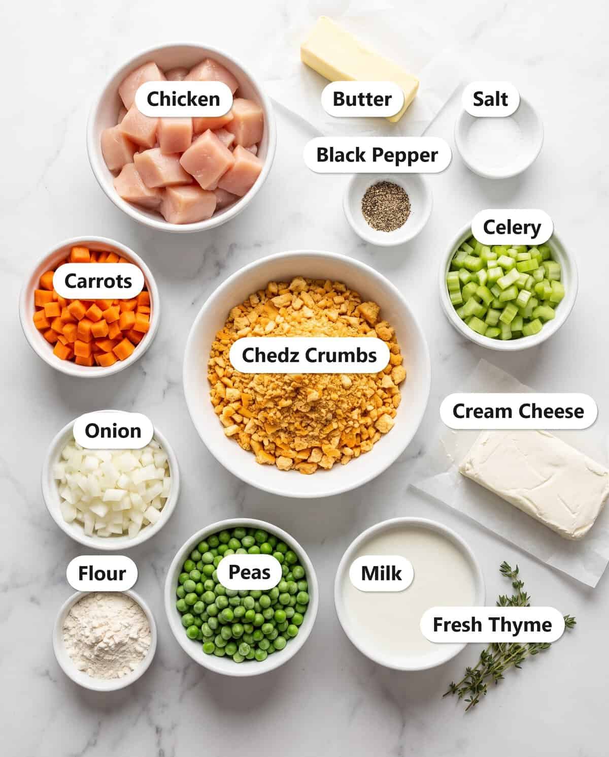 Chedz cheesy chicken pot pie ingredients including a bowl of orange Chedz crumbs, cubed chicken, carrots, celery, onion, peas, butter, cream cheese, flour, milk, and thyme.