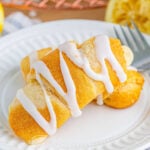 Lemon Cheesecake Crescent Rolls drizzled with lemon glaze on a white plate with fresh lemons.