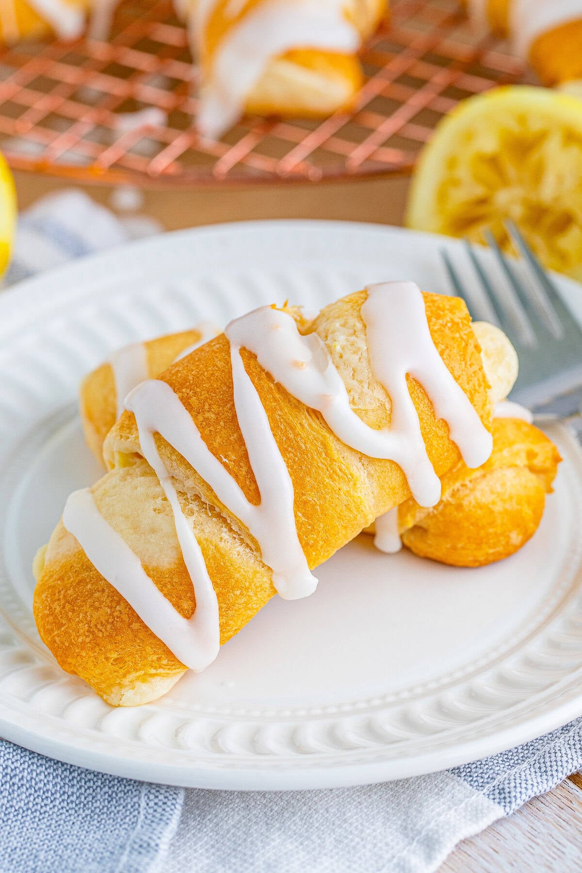 Lemon Cheesecake Crescent Rolls drizzled with lemon glaze on a white plate with fresh lemons.