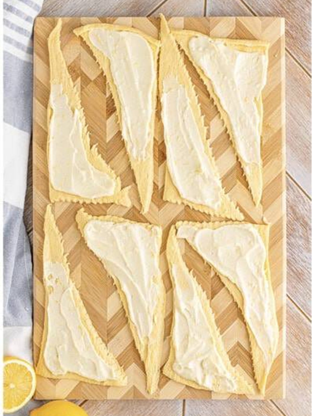 Rolled crescent rolls filled with lemon cheesecake on a parchment-lined baking sheet.