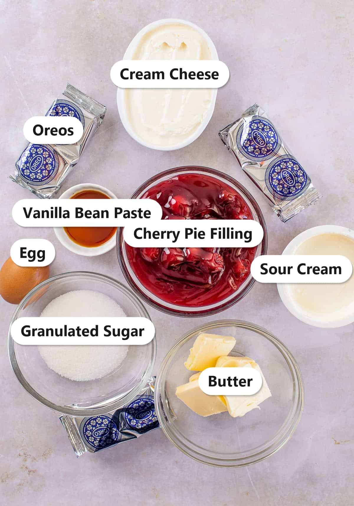 Labeled ingredients for cherry cheesecake bars including Oreos, cream cheese, sour cream, granulated sugar, butter, egg, vanilla bean paste, and cherry pie filling.