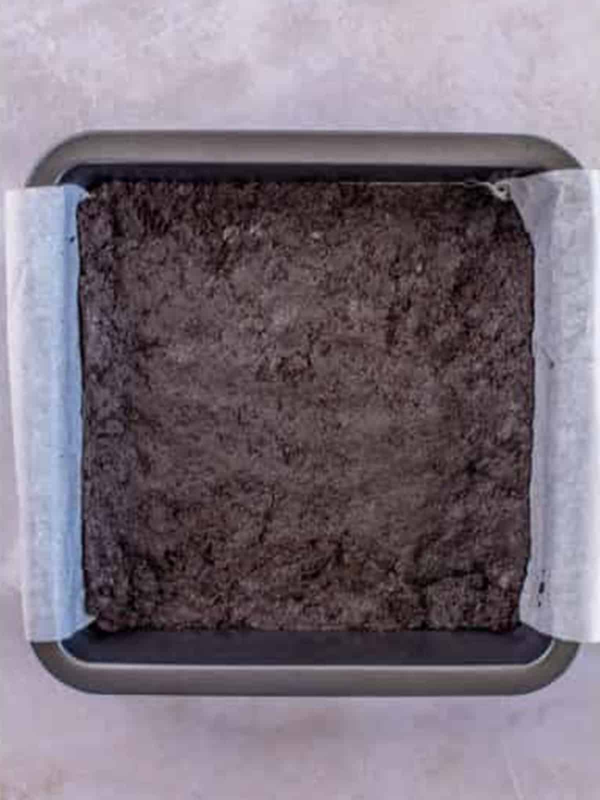 Oreo crust pressed evenly into a parchment lined square baking pan.
