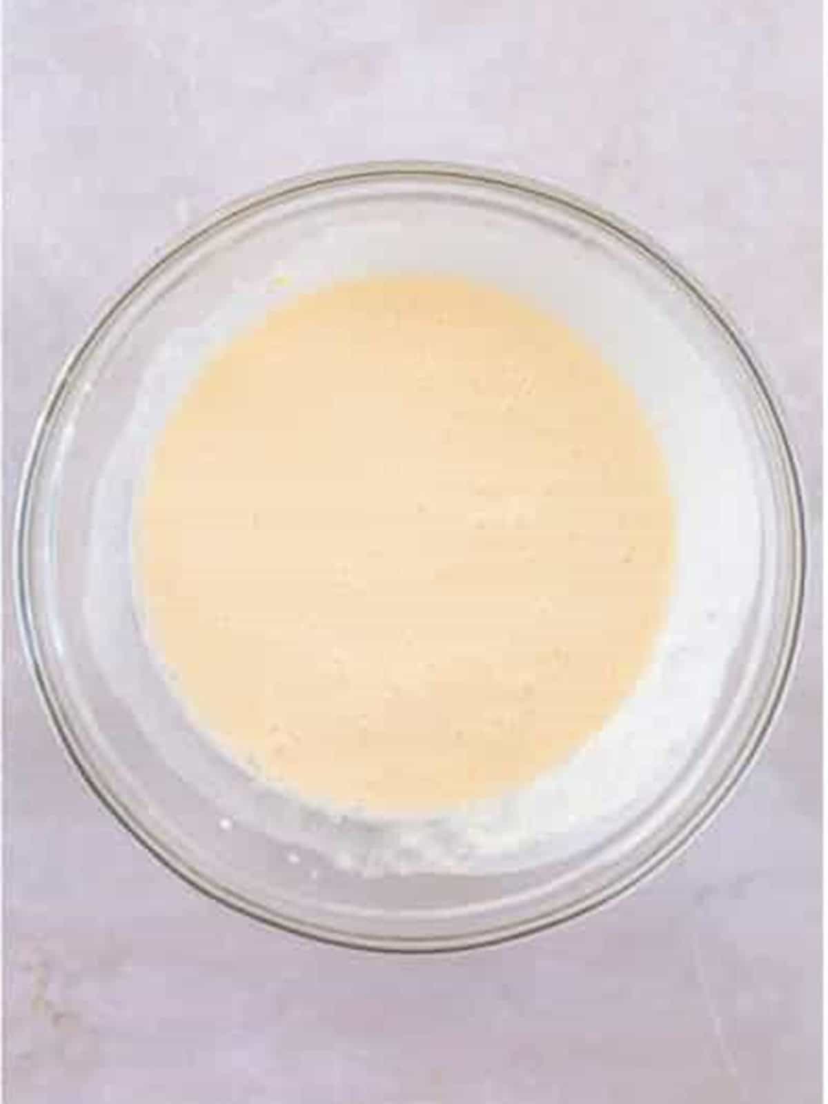Smooth cheesecake filling whisked together in a glass mixing bowl.