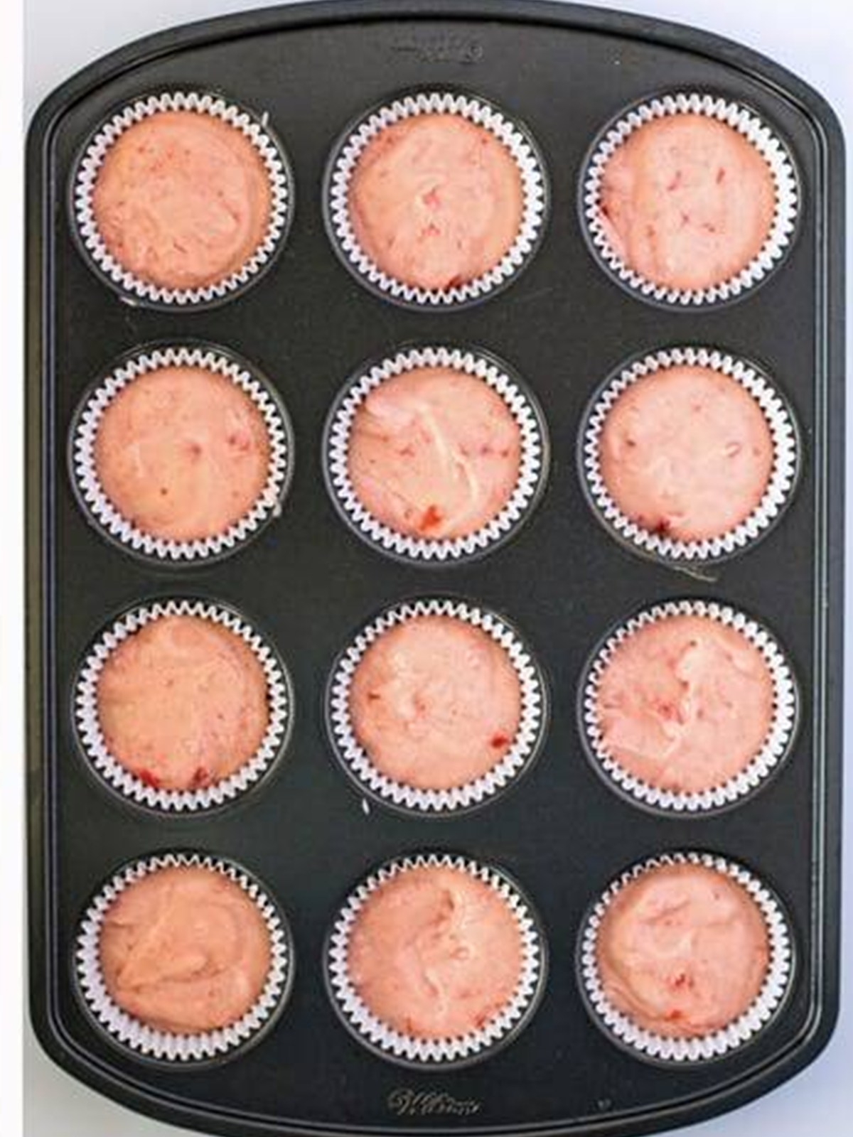 Cherry cupcake batter divided into a lined muffin tin ready to bake.