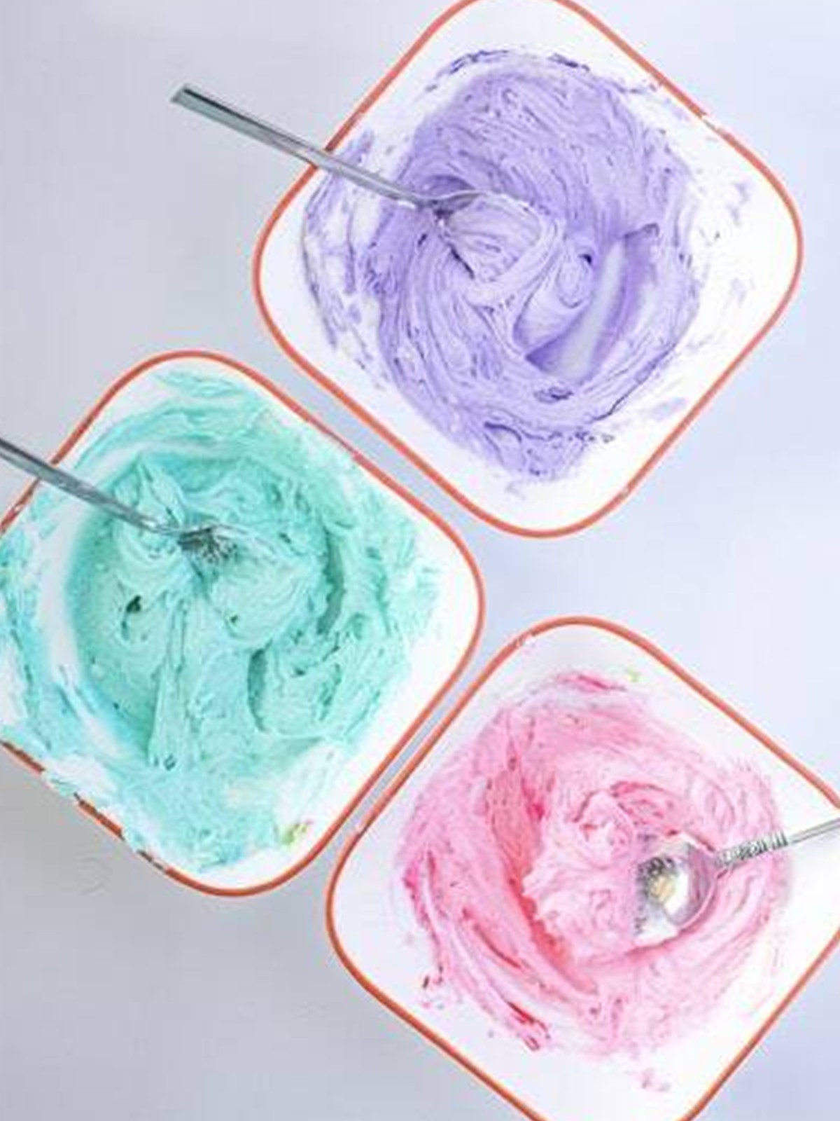 Frosting tinted pink, purple, and turquoise in three bowls for the tie dye swirl.
