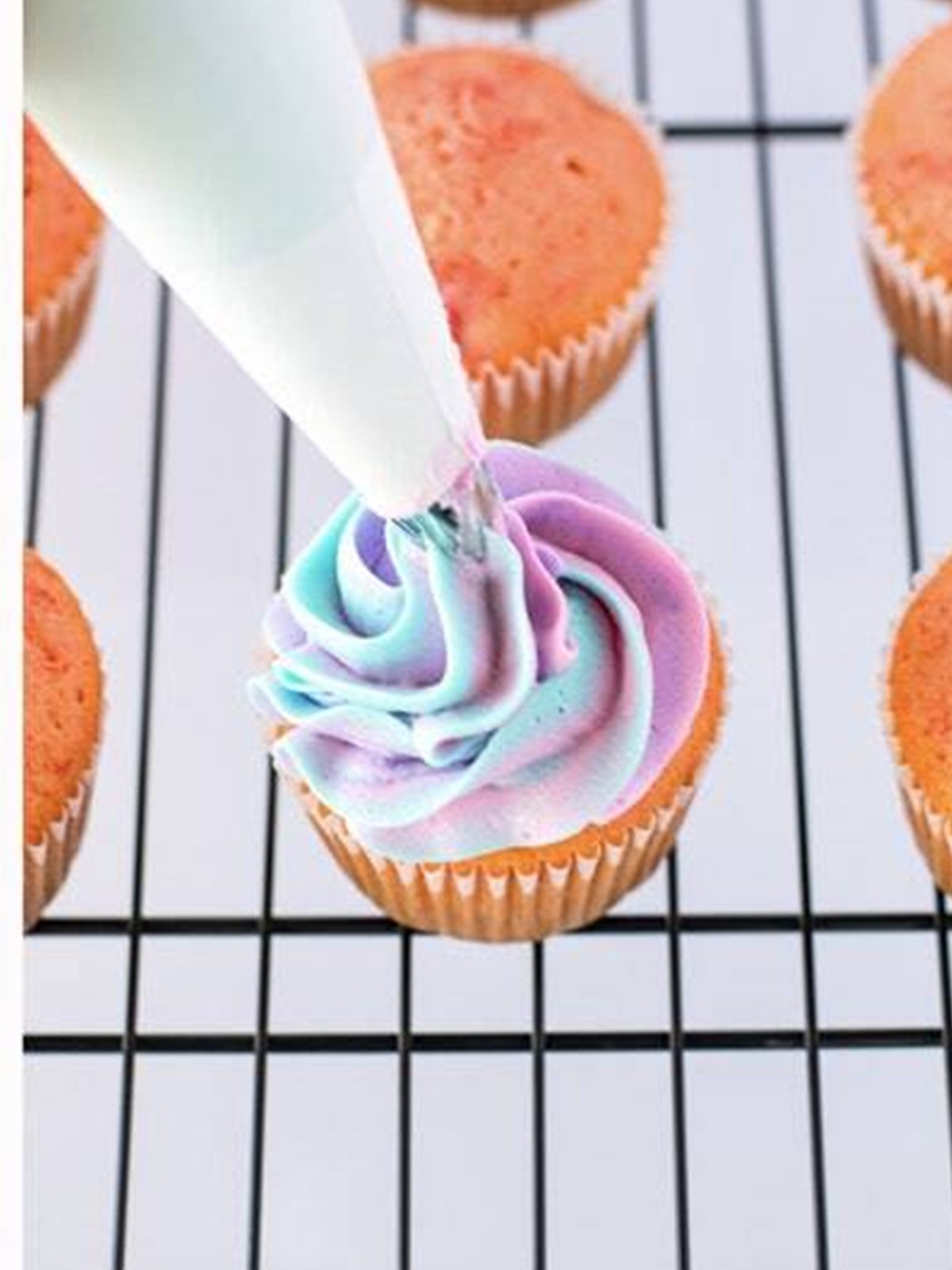 Piping the tie dye frosting swirl onto a cherry cupcake.