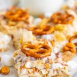 Chex Marshmallow Treats cut into squares and topped with pretzels on a tray with a glass of milk.