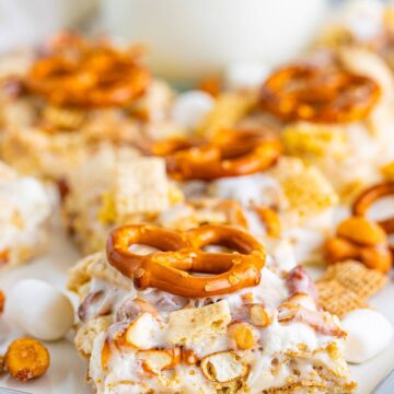 Chex Marshmallow Treats cut into squares and topped with pretzels on a tray with a glass of milk.