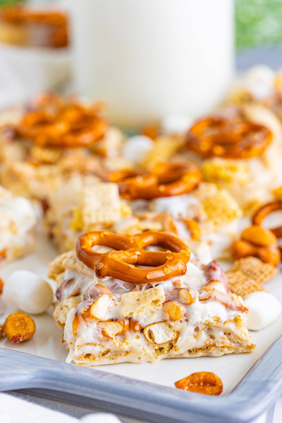 Chex Marshmallow Treats cut into squares and topped with pretzels on a tray with a glass of milk.