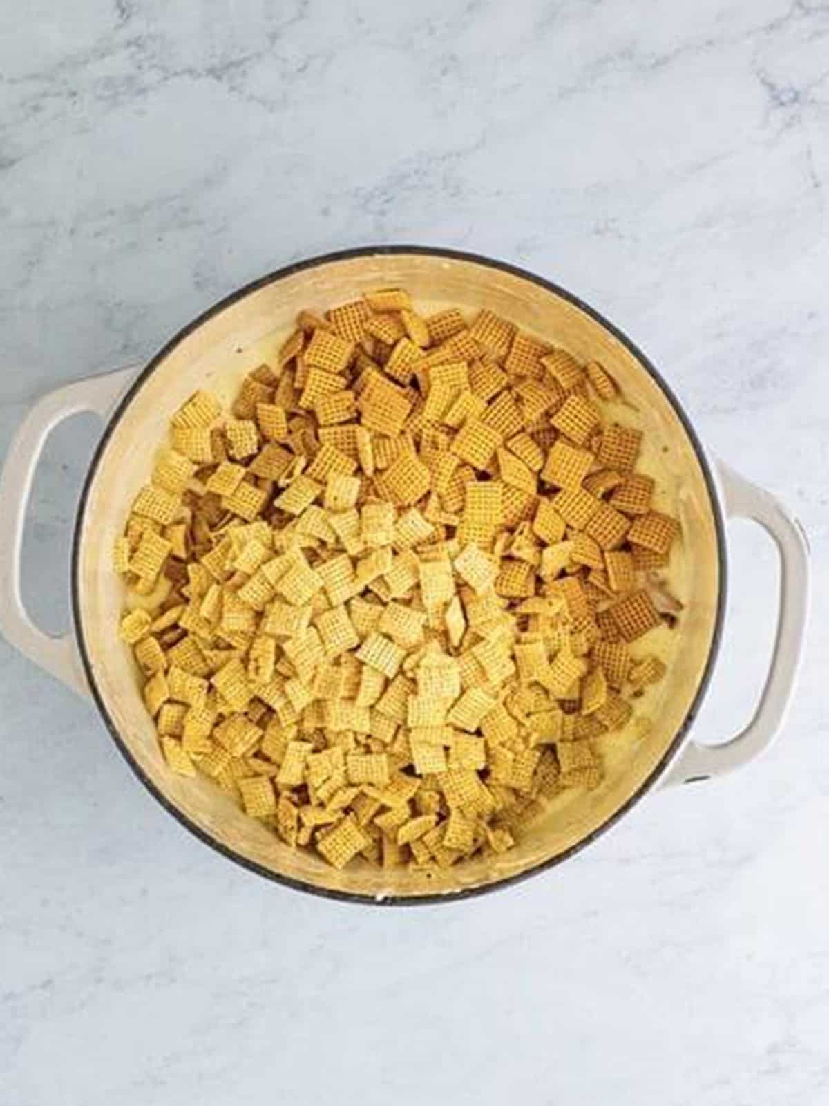 Stirring rice, corn, and wheat Chex cereal into the melted marshmallow mixture.