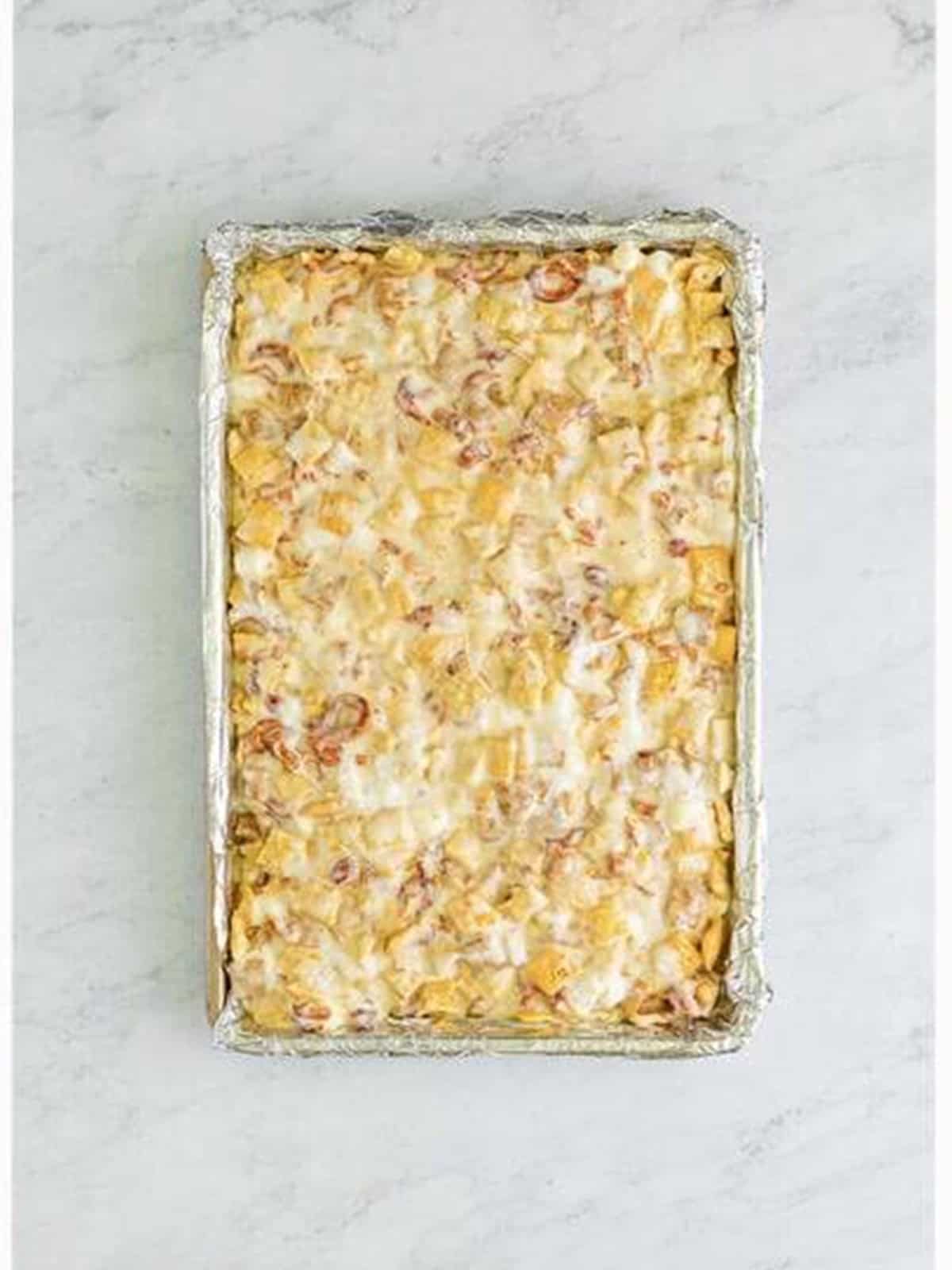 Pressing the Chex marshmallow mixture into a foil-lined baking pan.
