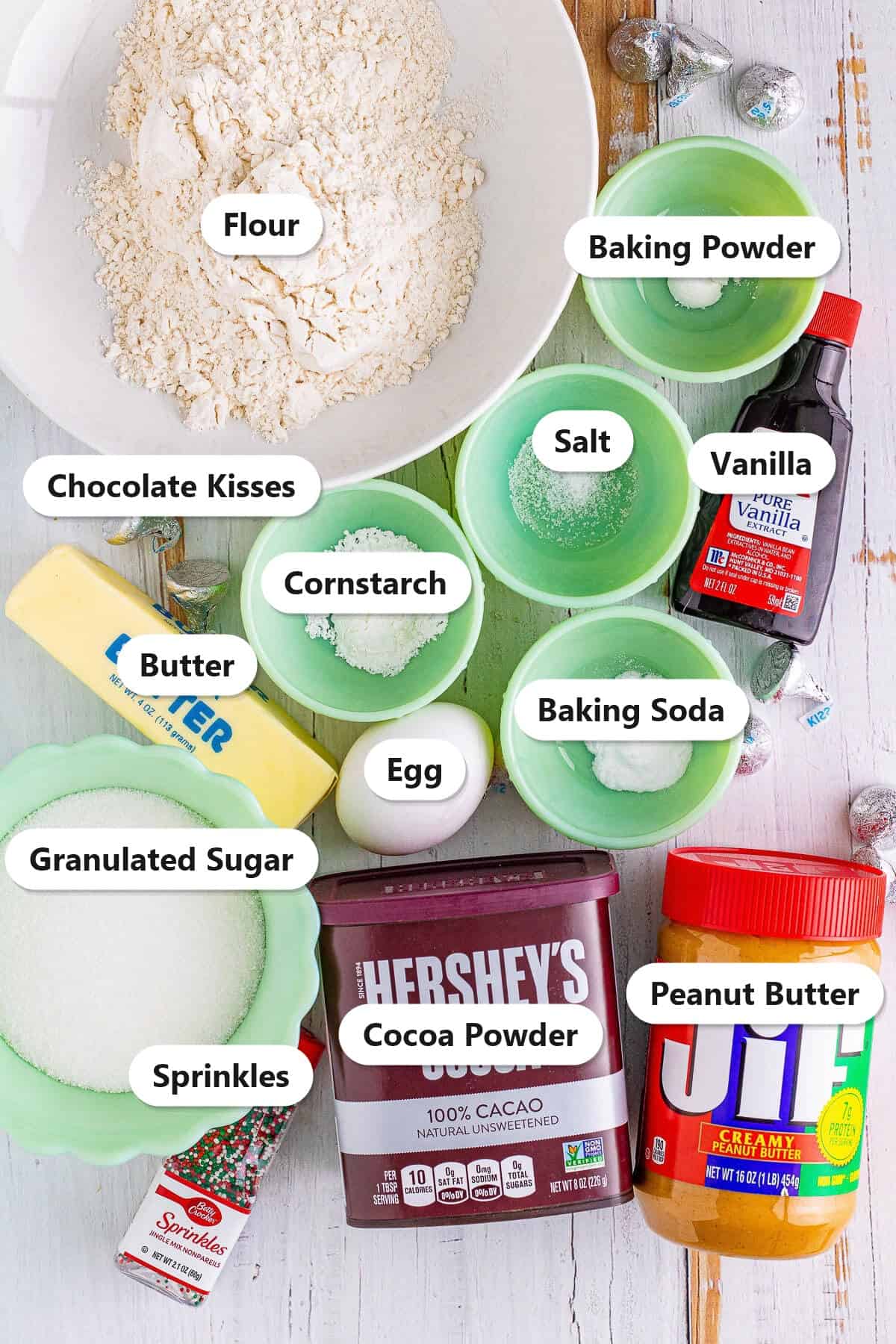 Labeled ingredients for chocolate blossom cookies including flour, cocoa powder, butter, granulated sugar, egg, peanut butter, vanilla, cornstarch, baking soda, baking powder, salt, sprinkles, and chocolate kisses.