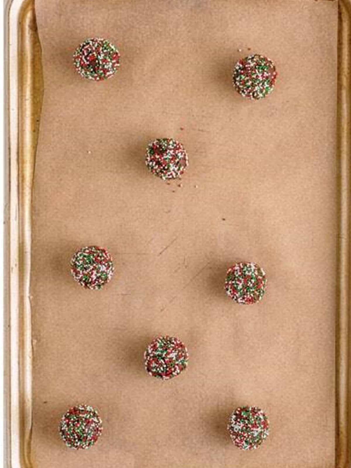 Chocolate cookie dough balls rolled in Christmas nonpareil sprinkles on a baking sheet.