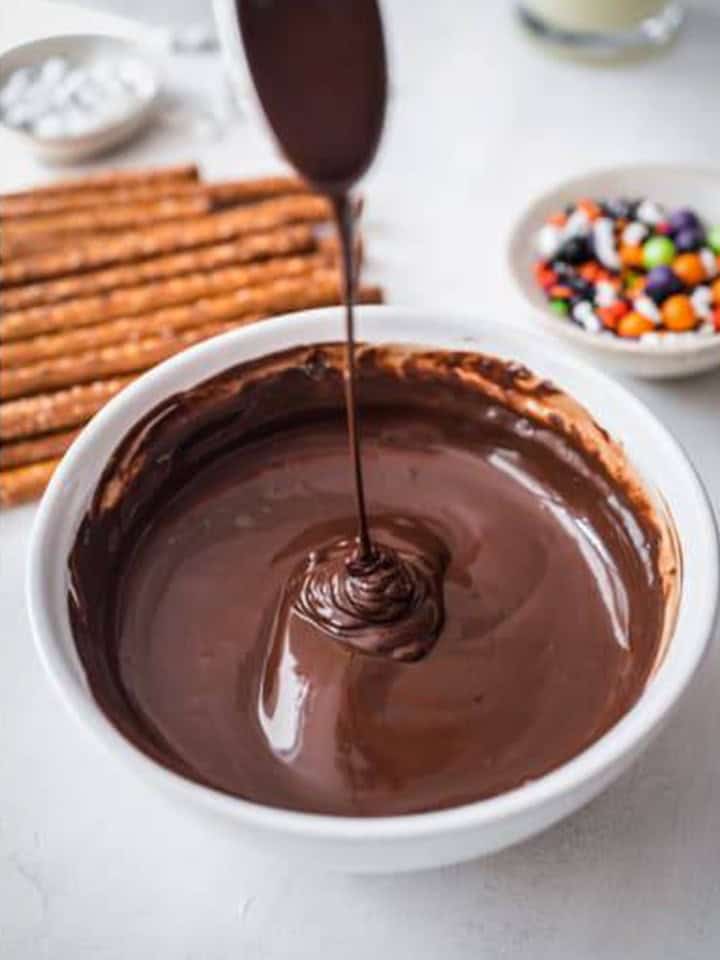 Melted semisweet chocolate dripping from a spoon into a white bowl.
