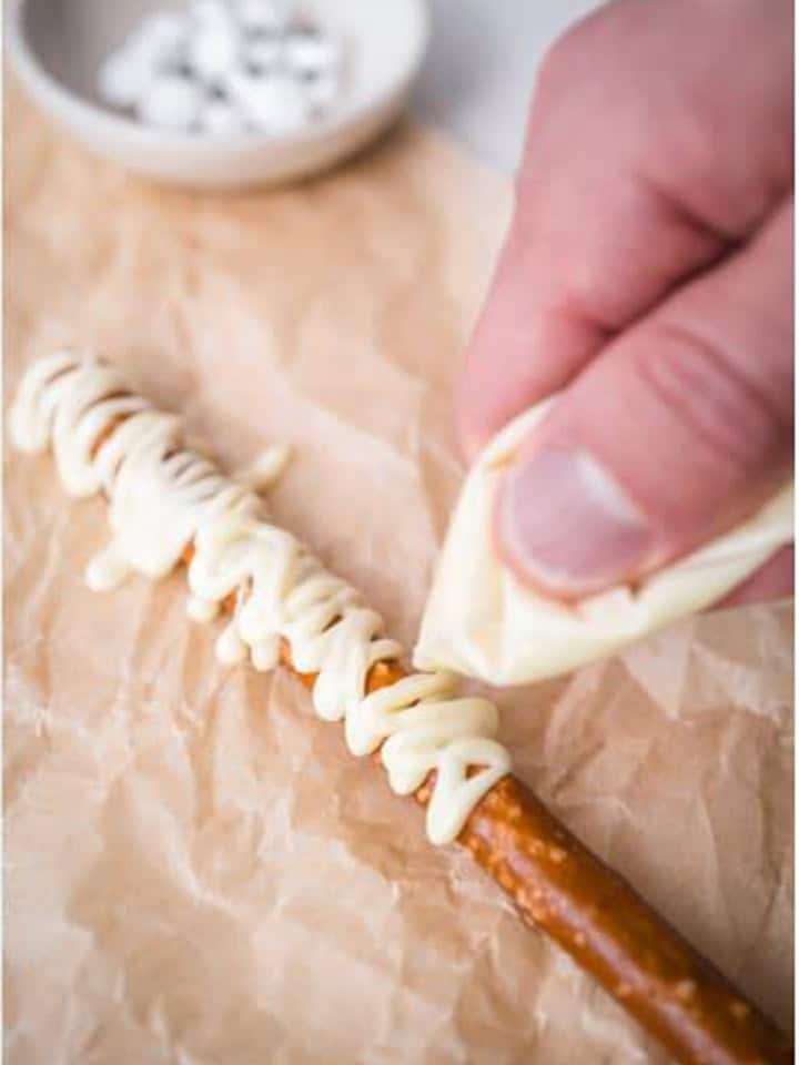 White chocolate being piped back and forth over a pretzel rod to look like mummy wrappings.