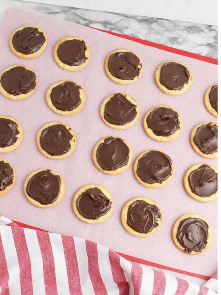 Mint chocolate frosting spread onto Ritz crackers arranged on a lined baking sheet.