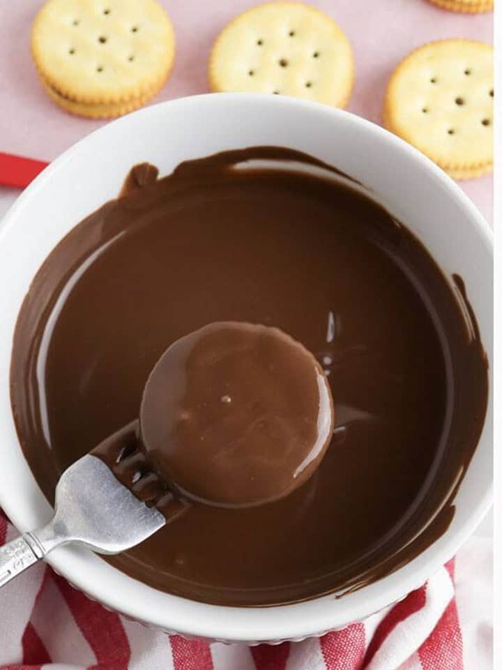 A Ritz cracker sandwich being dipped into a bowl of melted chocolate with a fork.