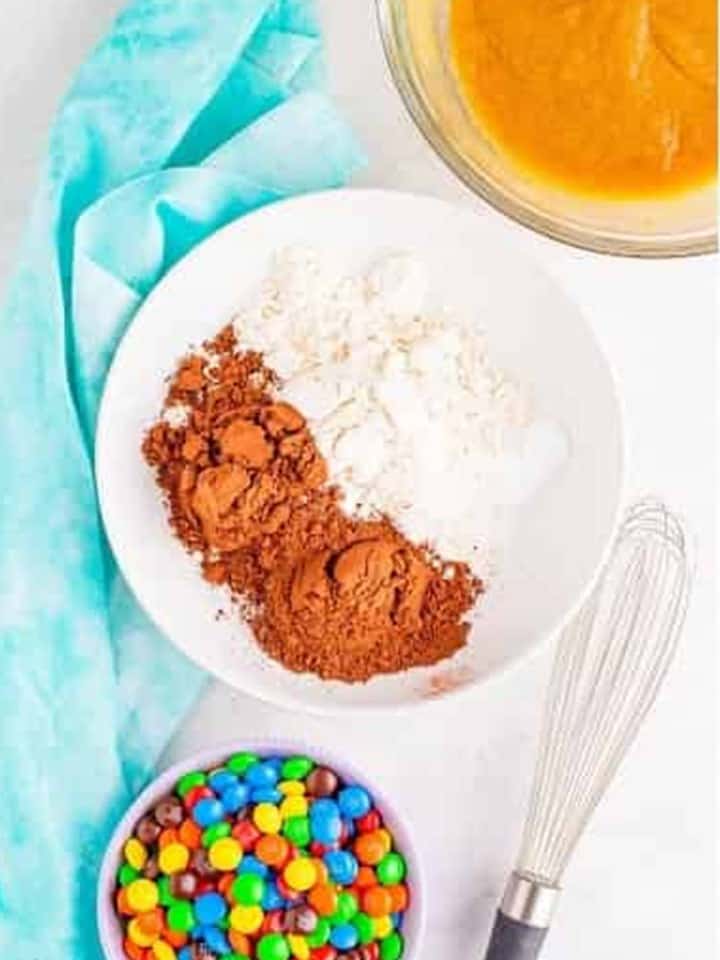 Flour, cocoa powder, baking soda, and salt in a bowl with a whisk for chocolate m&m cookies.