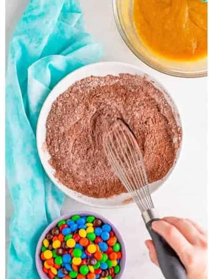 The dry ingredients whisked together for chocolate m&m cookies with a bowl of M&Ms nearby.