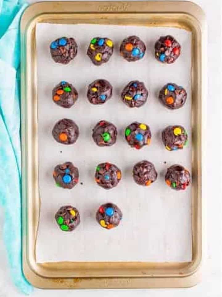 Chocolate m&m cookie dough balls arranged on a parchment lined sheet tray to chill.