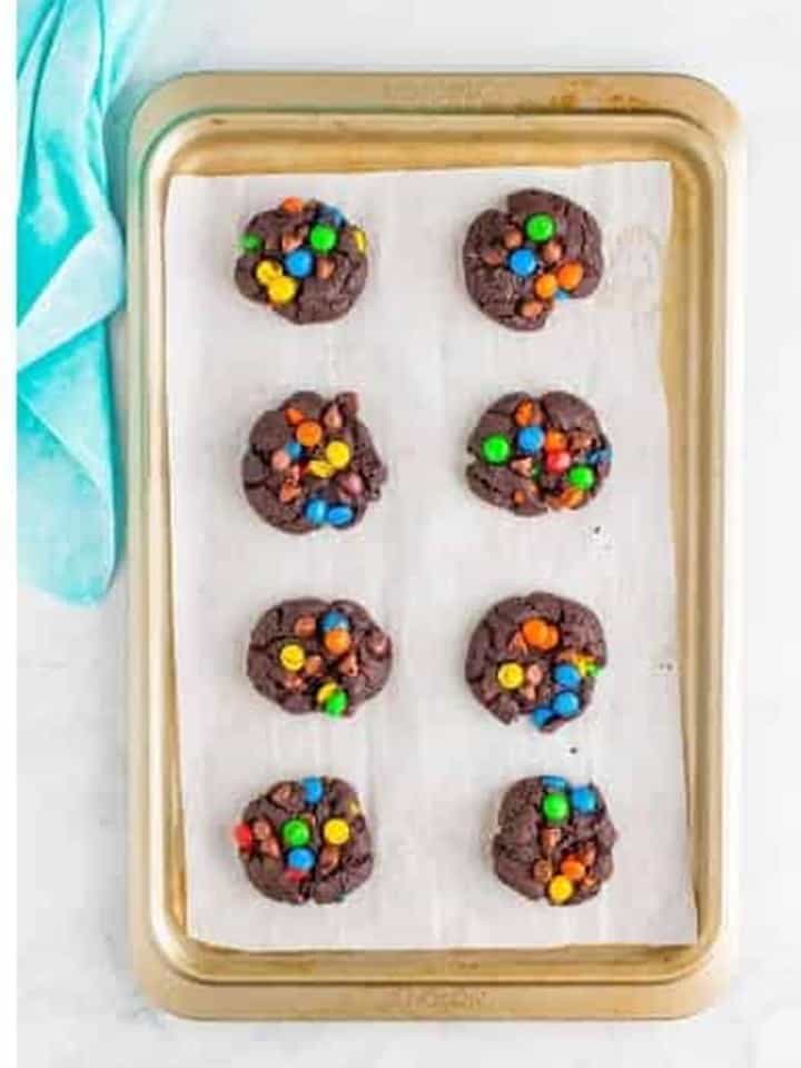 Chilled chocolate m&m cookie dough balls spaced on the tray and pressed slightly flat before baking.