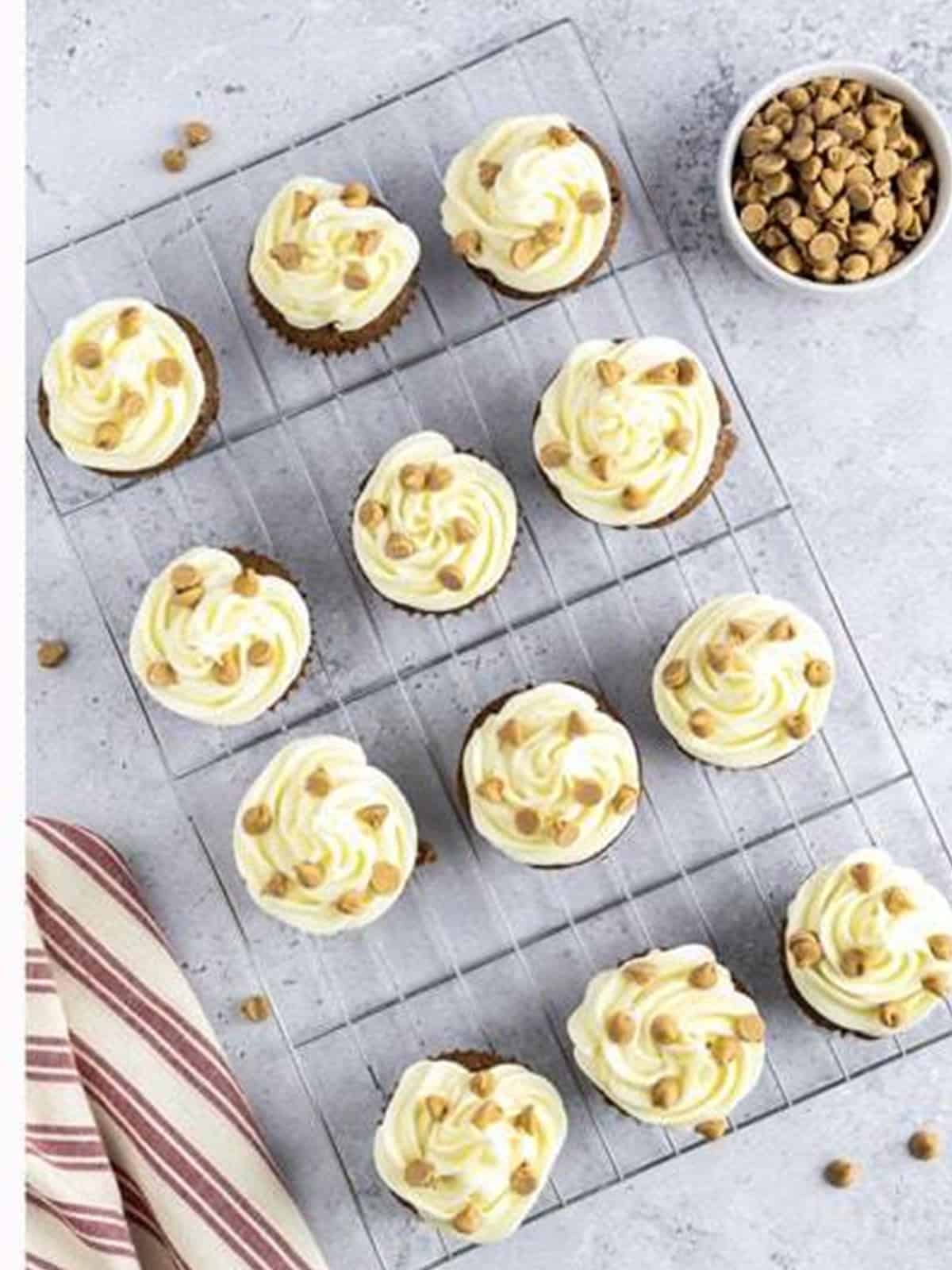 Frosted chocolate peanut butter cupcakes garnished with peanut butter chips on a wire rack.