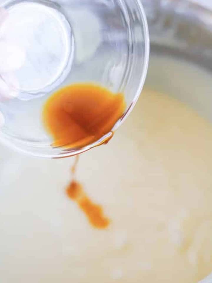 Vanilla extract being poured into the melted white chocolate fudge base for christmas fudge.