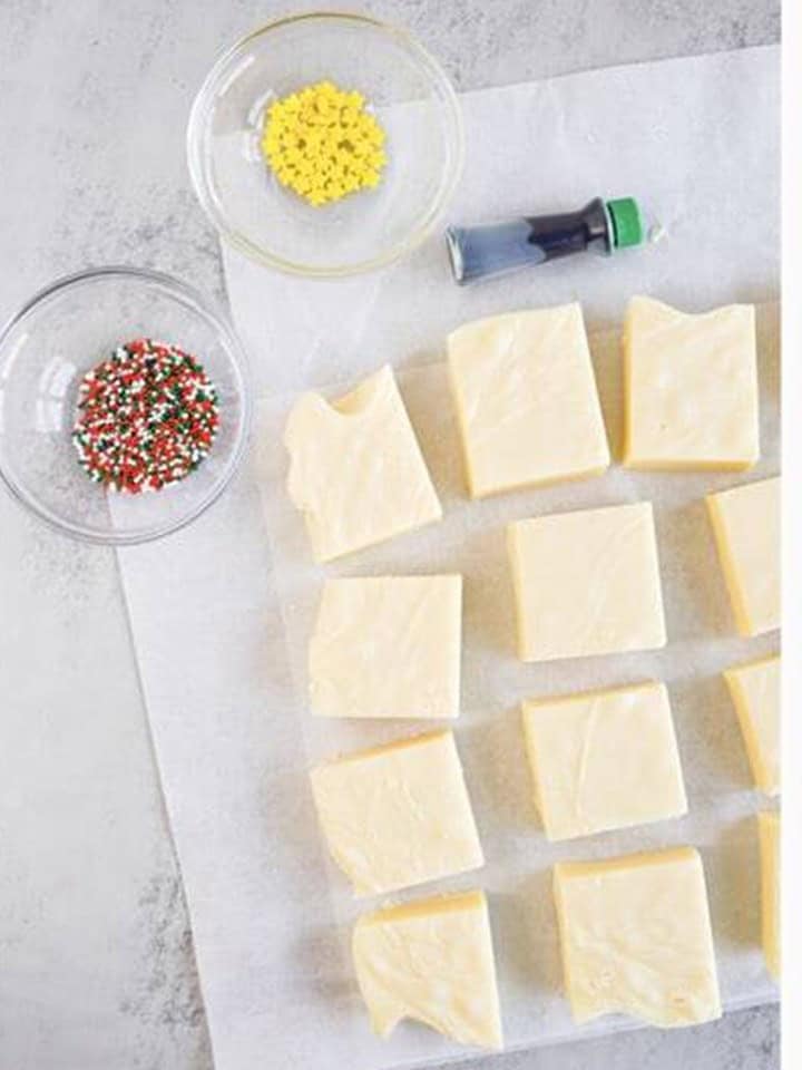 Set christmas fudge cut into sixteen squares on parchment paper with decorating supplies nearby.