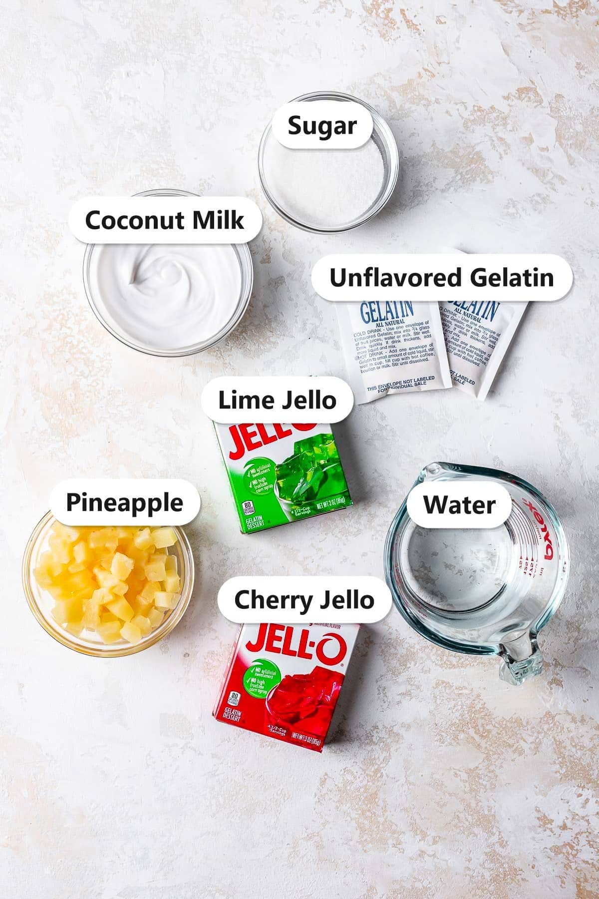 Labeled ingredients for Christmas jello salad including cherry jello, lime jello, pineapple, coconut milk, unflavored gelatin, sugar, and water.