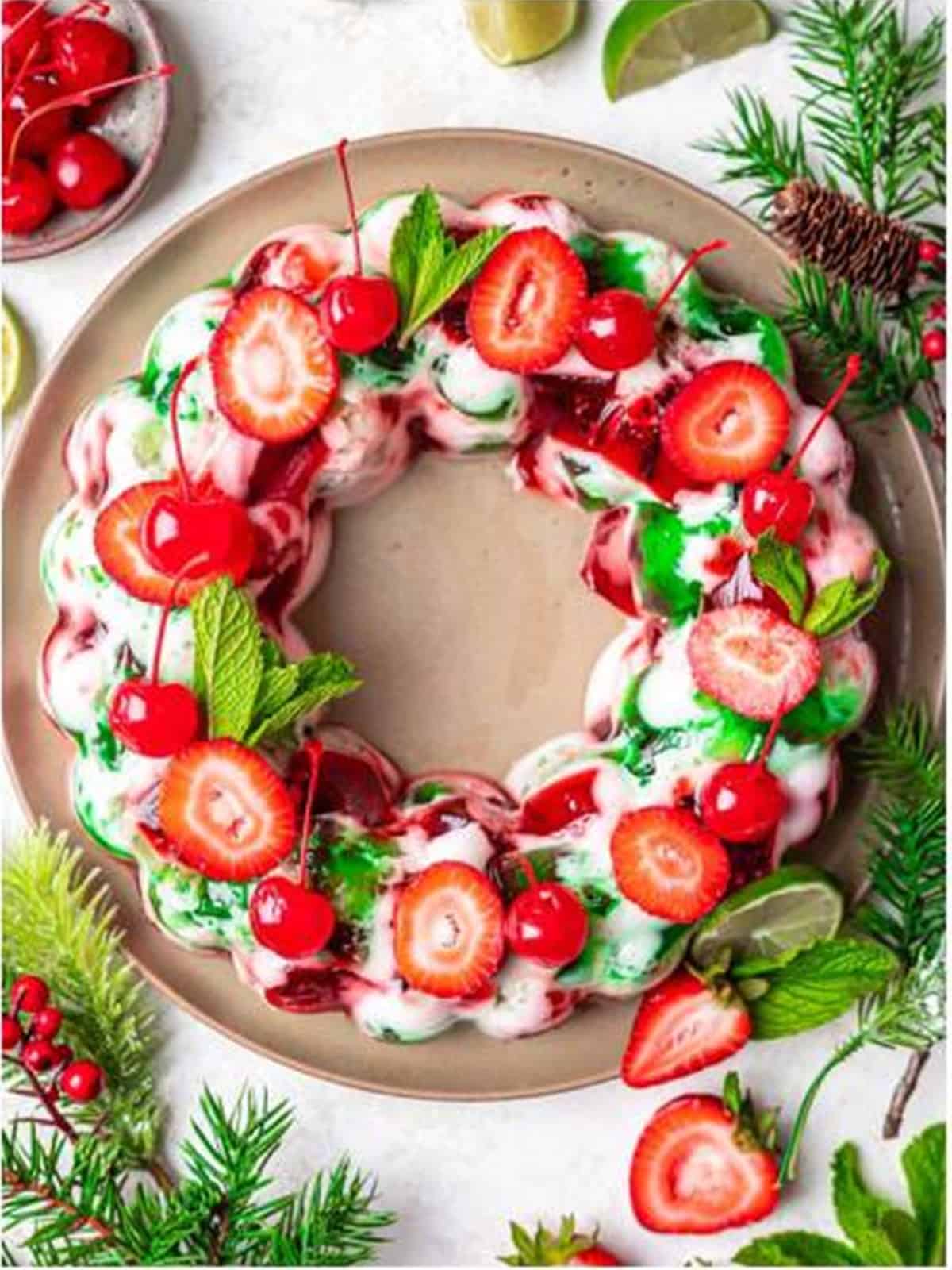 An unmolded Christmas jello salad wreath garnished with cherries, strawberries, and mint.