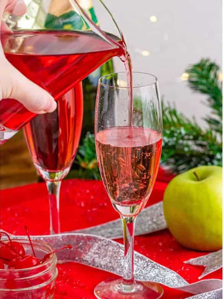 Cranberry apple juice being poured into the flute turning the Christmas Mocktail festive red.