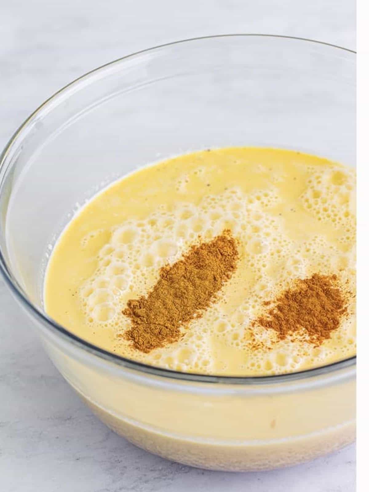 Pumpkin pie spice and cinnamon added on top of eggnog in a large glass mixing bowl for Christmas punch.