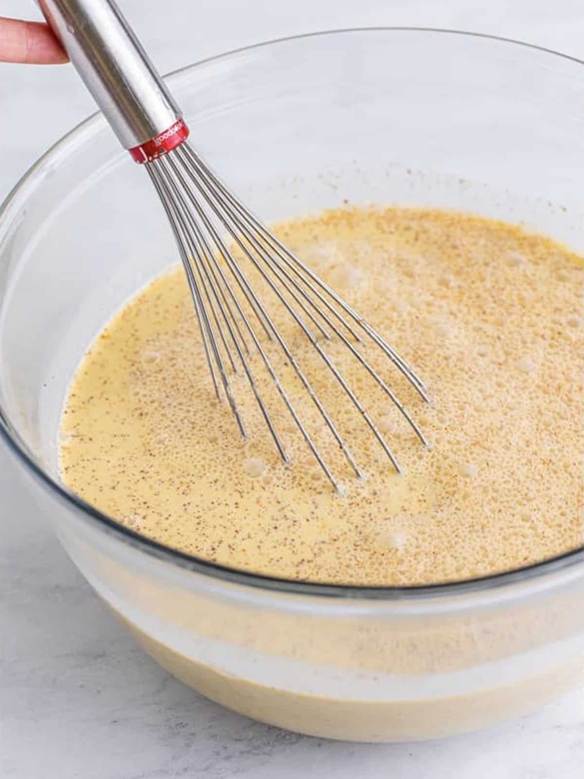 Whisking the eggnog, Fireball, and spices together in a glass bowl until the Christmas punch is smooth.